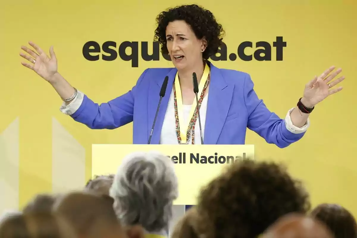 Marta Rovira con chaqueta azul y camiseta blanca gesticula con las manos levantadas mientras habla en un podio amarillo con la inscripción "Consell Nacional" frente a un fondo amarillo con el texto "esquerra.cat".