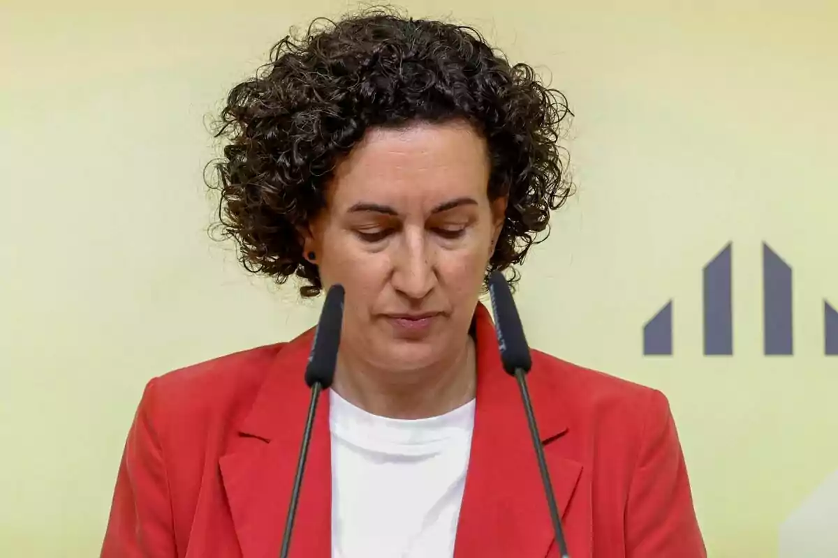 Marta Rovira con chaqueta roja hablando frente a dos micrófonos.