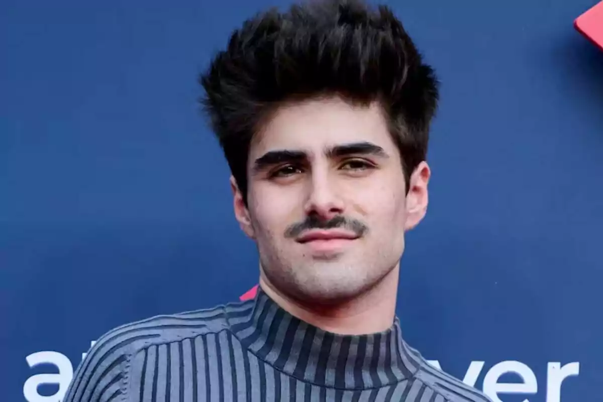 Fotografía de Martin Urrutia con bigote y cabello oscuro, vistiendo un suéter de rayas grises, posando frente a un fondo azul.