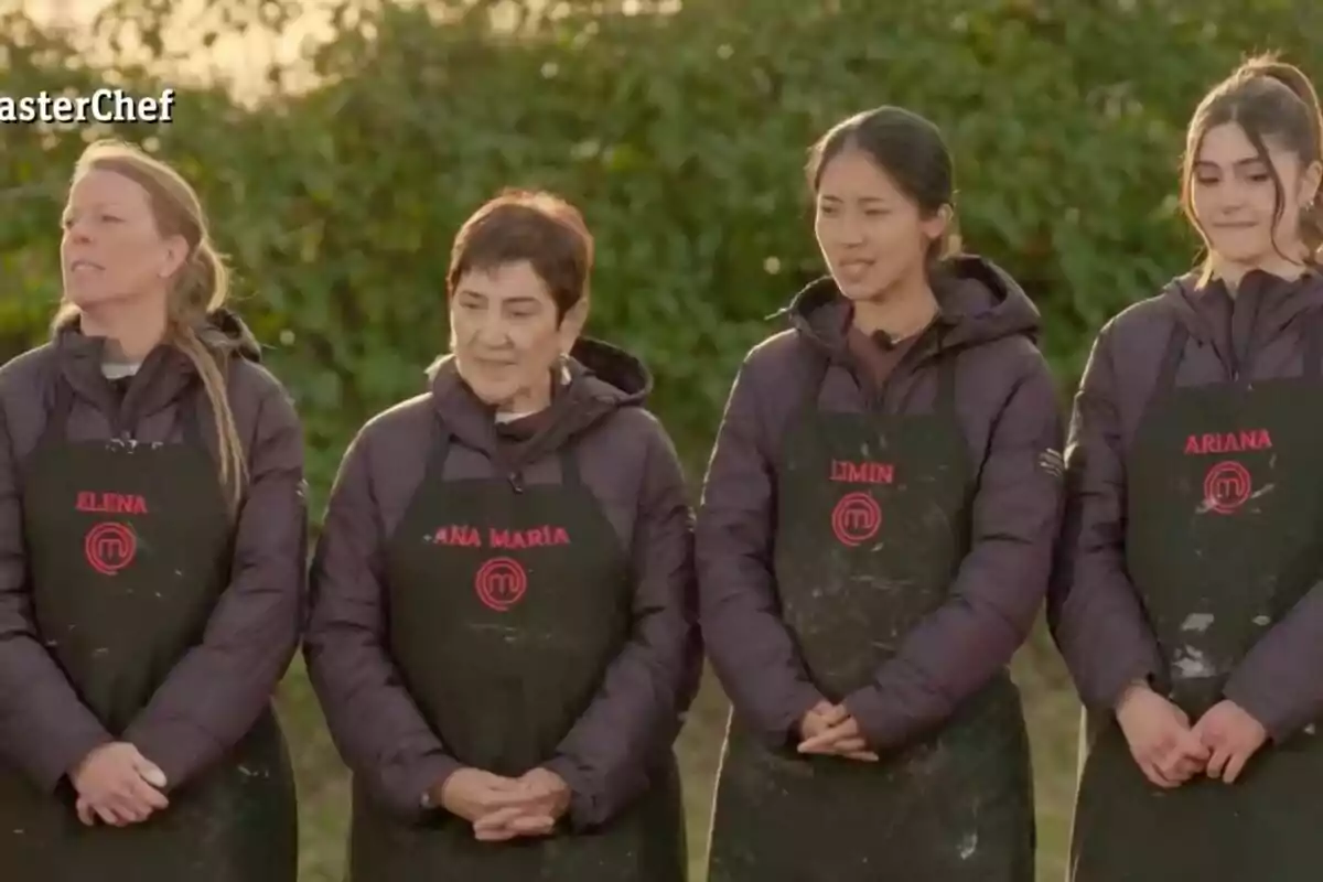 Un grupo de cuatro personas vestidas con delantales negros y chaquetas oscuras, de pie al aire libre frente a un fondo de vegetación en 'Masterchef'. Un grupo de cuatro personas vestidas con delantales negros y chaquetas oscuras, de pie al aire libre frente a un fondo de vegetación en 'Masterchef'.