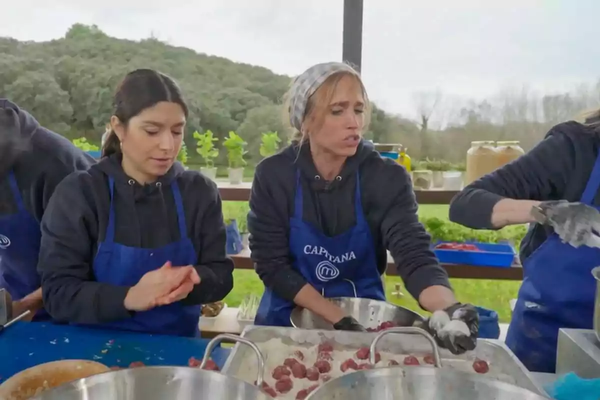 Dos mujeres con delantales azules preparan albóndigas en una cocina al aire libre rodeada de vegetación en 'Masterchef'. Dos mujeres con delantales azules preparan albóndigas en una cocina al aire libre rodeada de vegetación en 'Masterchef'.