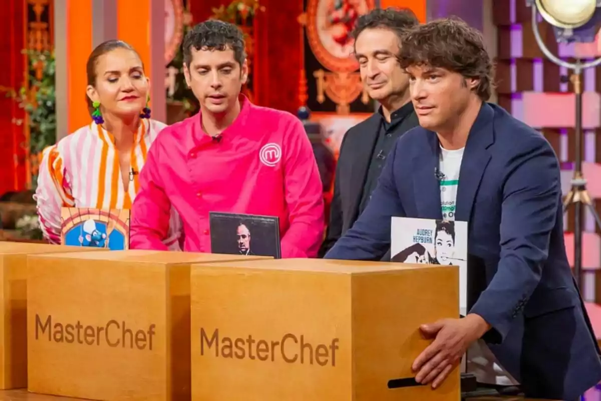 Jordi Cruz, Pepe Rodríguez y Samantha Vallejo Nágera junto a Eduardo Casanova están de pie detrás de cajas de madera con el logo de MasterChef en un set de televisión colorido.