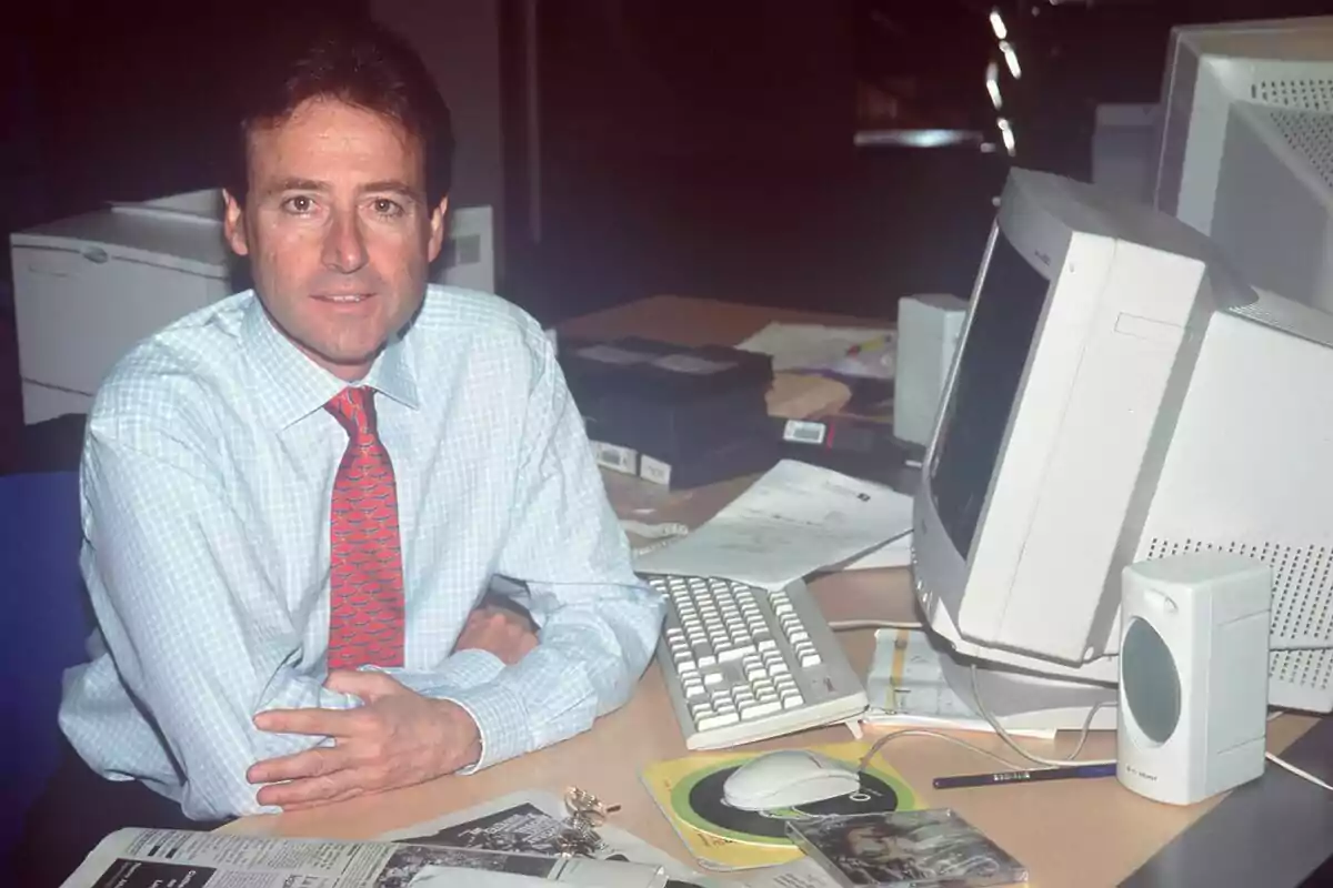 Matías Prats con camisa blanca y corbata roja está sentado en un escritorio con una computadora antigua, teclado, ratón y varios papeles en Antena 3 Noticias. Matías Prats con camisa blanca y corbata roja está sentado en un escritorio con una computadora antigua, teclado, ratón y varios papeles en Antena 3 Noticias.
