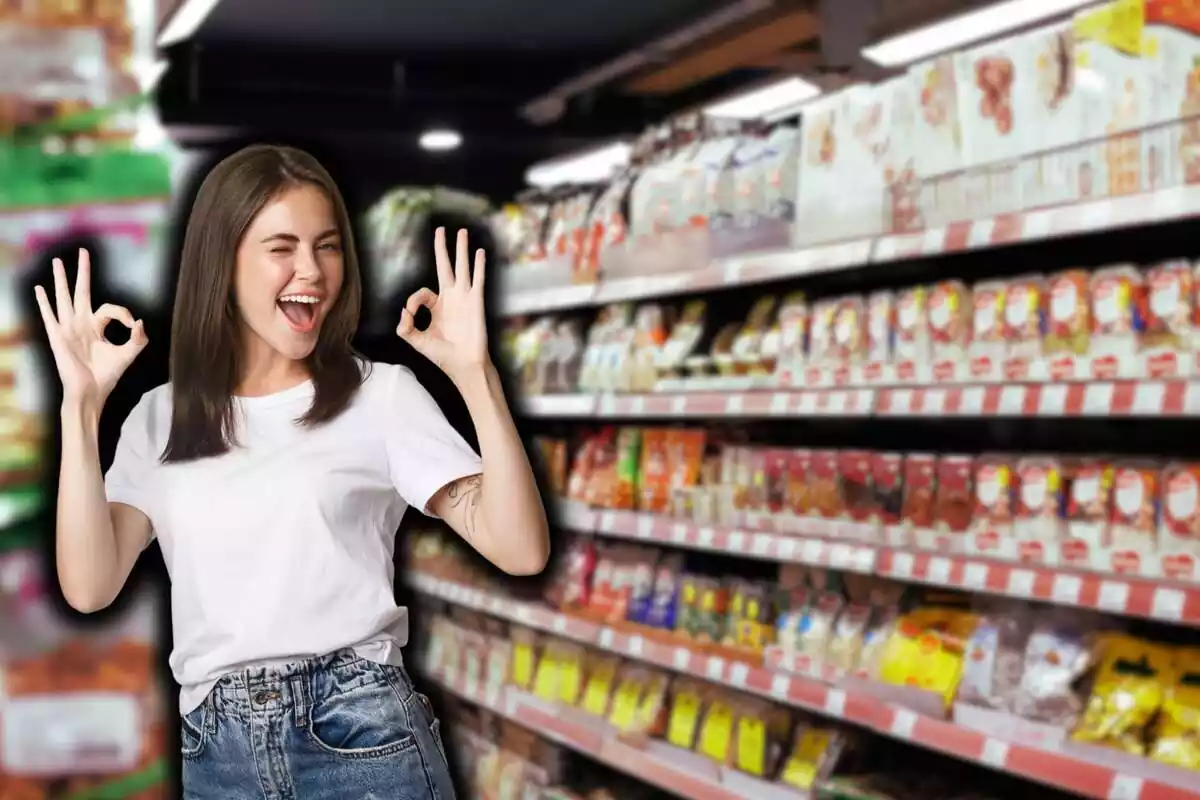Chica morena camiseta blanca y vaqueros, guiñando y haciendo el signo de ok con ambas manos, sobre fondo de supermercado desenfocado