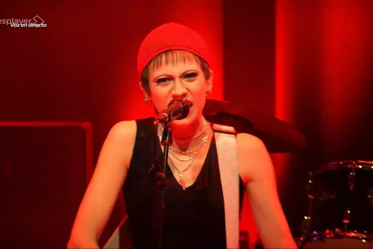 Melani cantando en el escenario con luz roja de fondo y expresión intensa mientras sostiene una guitarra eléctrica en Tu Cara Me Suena Melani cantando en el escenario con luz roja de fondo y expresión intensa mientras sostiene una guitarra eléctrica en Tu Cara Me Suena