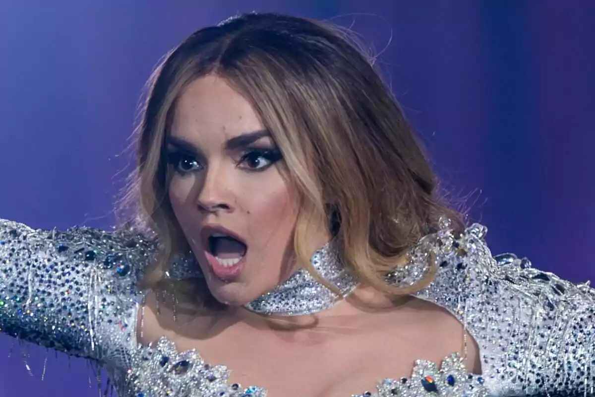 Melody con expresión de sorpresa en el escenario de Eurovisión, vestida con un traje brillante y decorado con pedrería.