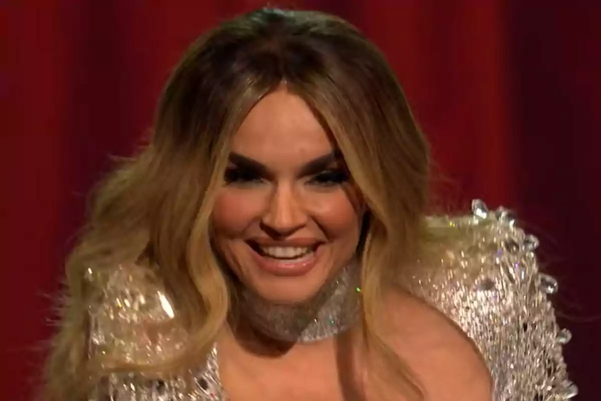 Melody con cabello largo y rubio sonriendo y vistiendo un atuendo brillante frente a un fondo rojo en la final de Eurovisión.