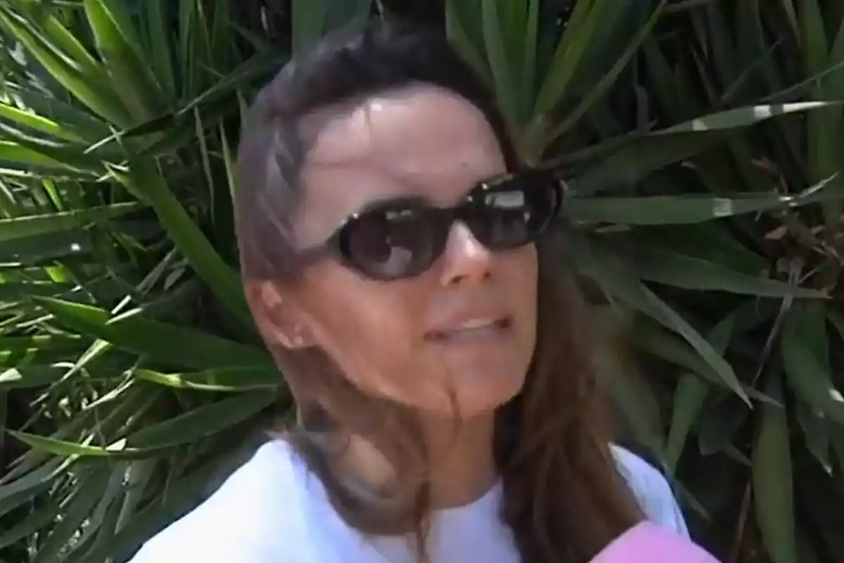 Melody con gafas de sol hablando frente a un micrófono rosa con plantas verdes de fondo en Vamos a ver.