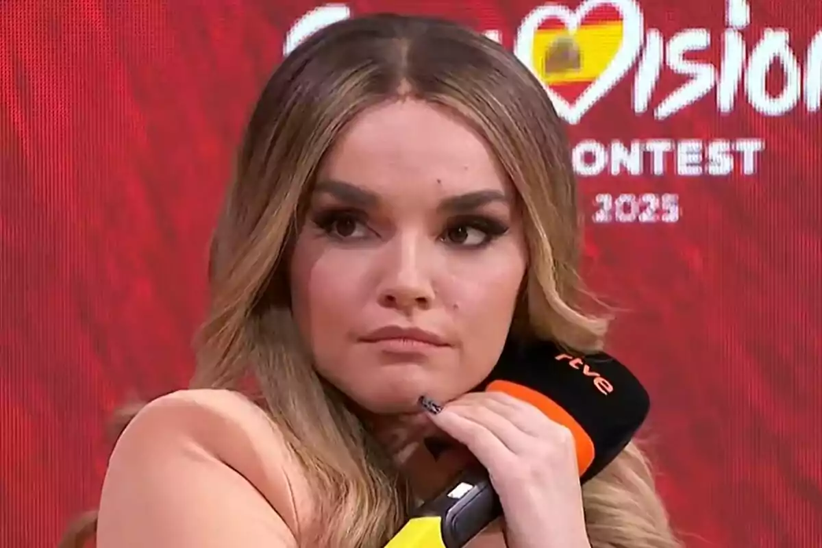 Melody de cabello largo y rubio sosteniendo un micrófono negro y naranja con fondo rojo y letras blancas de un concurso de música de Eurovisión.