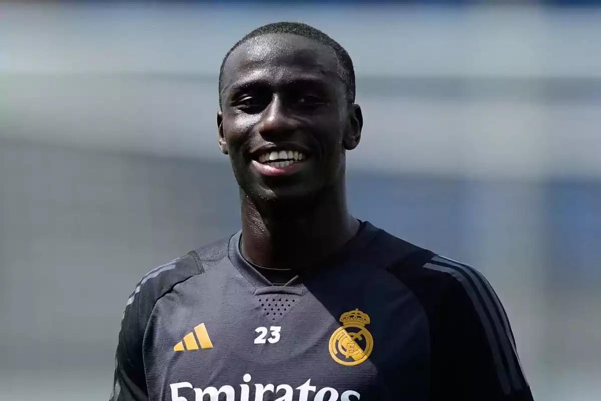 Jugador de fútbol sonriendo con el uniforme de entrenamiento del Real Madrid.