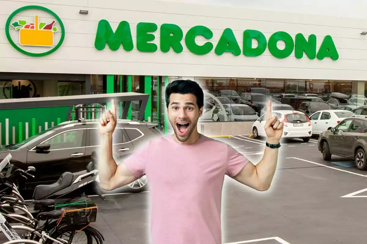 Un hombre sonriente con una camiseta rosa señala hacia arriba con ambas manos frente a una tienda de Mercadona.