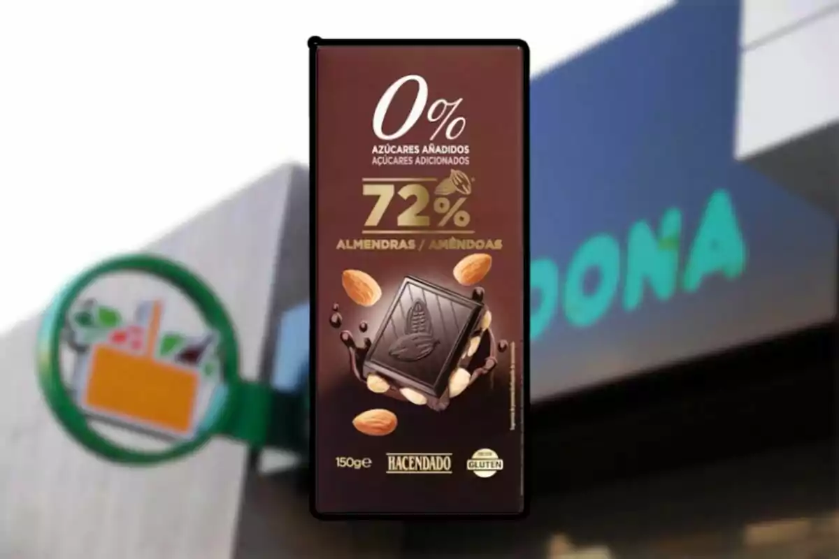 Un paquete de chocolate negro con almendras de la marca Hacendado, con 72% de cacao y sin azúcares añadidos, frente a un fondo borroso de un supermercado. Un paquete de chocolate negro con almendras de la marca Hacendado, con 72% de cacao y sin azúcares añadidos, frente a un fondo borroso de un supermercado.