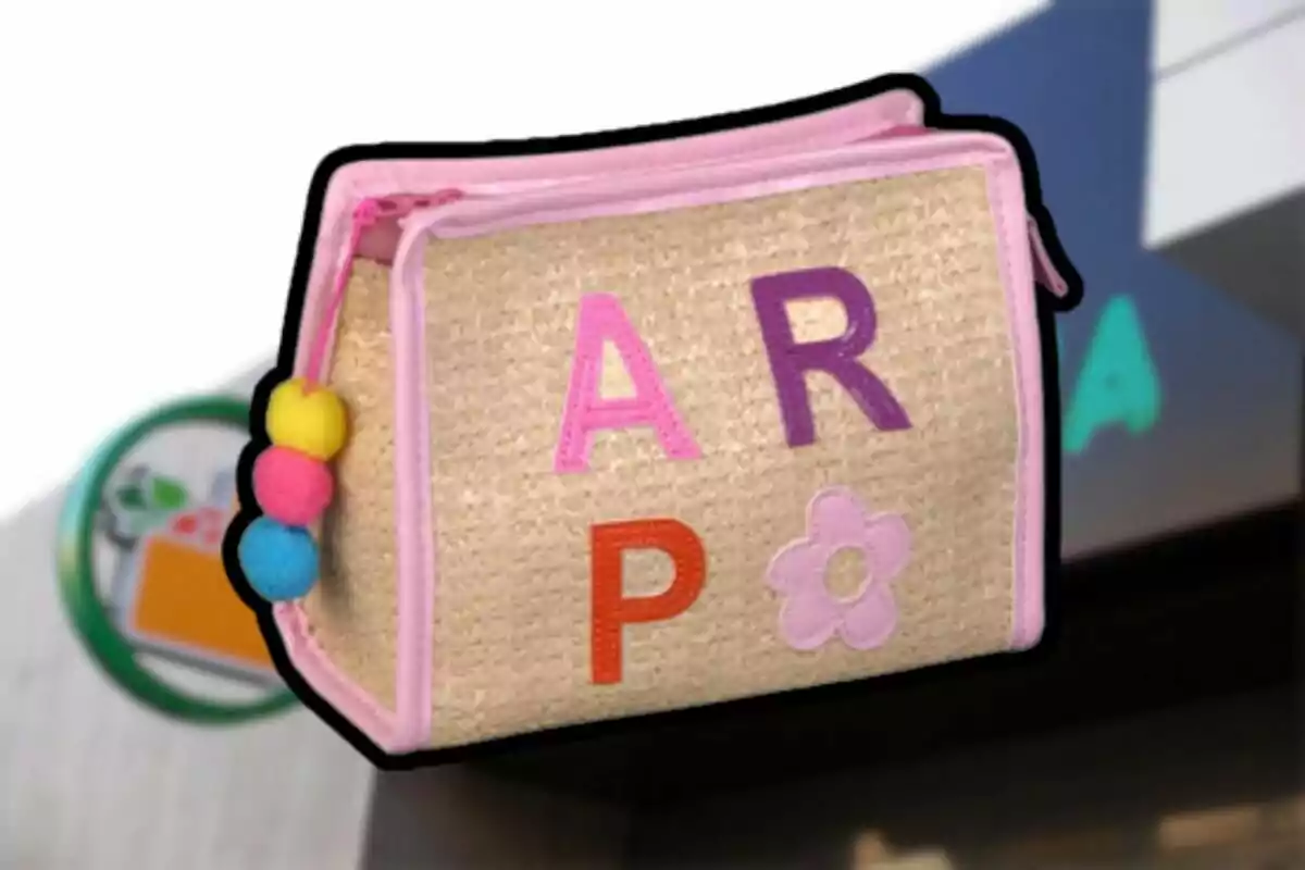 Una bolsa de tela beige con bordes rosados y letras de colores, adornada con pompones de colores en un lateral. Una bolsa de tela beige con bordes rosados y letras de colores, adornada con pompones de colores en un lateral.