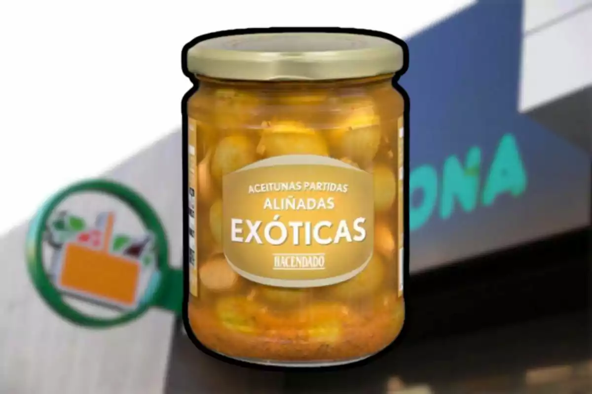 Frasco de aceitunas partidas aliñadas exóticas de la marca Hacendado frente a un cartel de supermercado Mercadona desenfocado Frasco de aceitunas partidas aliñadas exóticas de la marca Hacendado frente a un cartel de supermercado Mercadona desenfocado