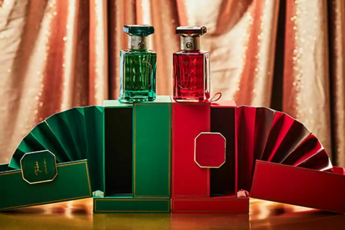 Dos frascos de perfume, uno verde y otro rojo, sobre cajas decorativas a juego con un fondo de cortinas doradas. Dos frascos de perfume, uno verde y otro rojo, sobre cajas decorativas a juego con un fondo de cortinas doradas.