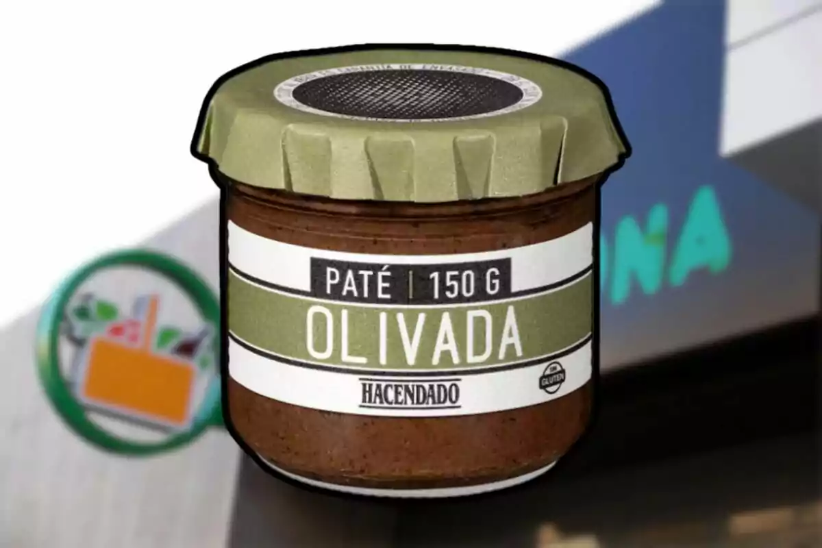 Un frasco de paté de olivada de la marca Hacendado con un fondo que muestra parte de un logotipo de supermercado. Un frasco de paté de olivada de la marca Hacendado con un fondo que muestra parte de un logotipo de supermercado.