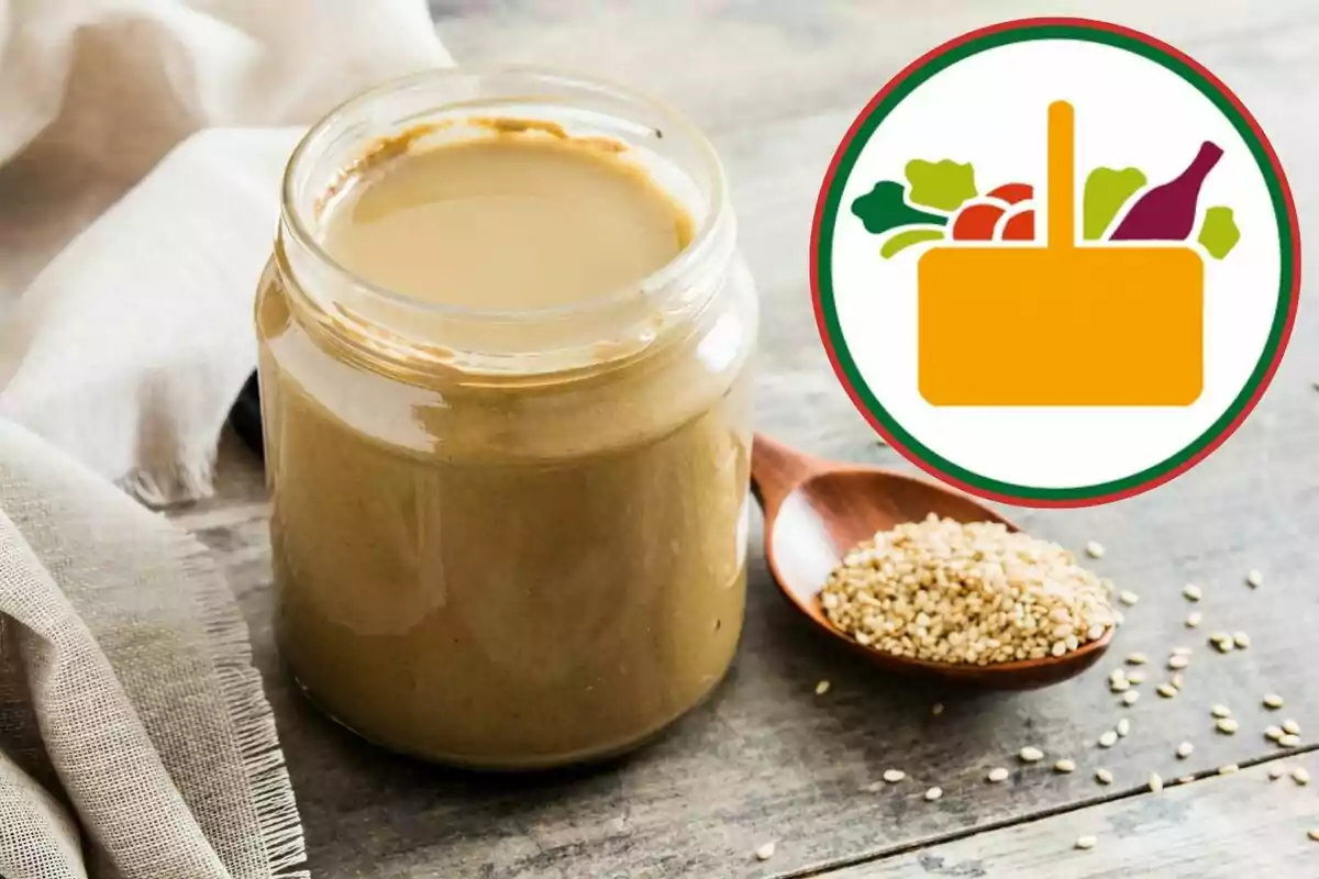 Frasco de crema de sésamo sobre una mesa de madera junto a una cuchara con semillas y un icono de canasta de alimentos Frasco de crema de sésamo sobre una mesa de madera junto a una cuchara con semillas y un icono de canasta de alimentos
