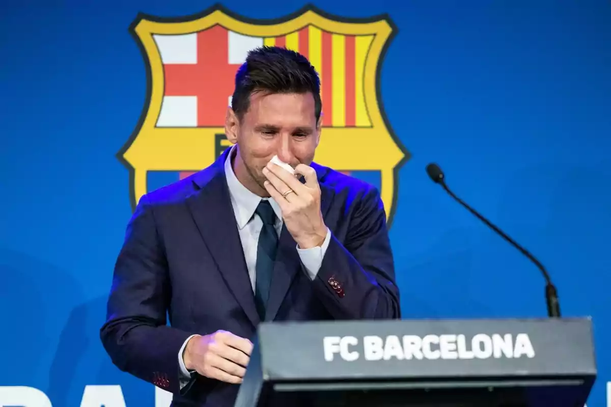 Un hombre en traje oscuro se limpia las lágrimas con un pañuelo frente a un podio con el logo del FC Barcelona. Un hombre en traje oscuro se limpia las lágrimas con un pañuelo frente a un podio con el logo del FC Barcelona.
