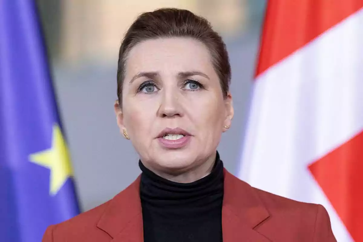 Una persona hablando frente a banderas de la Unión Europea y de otro país.