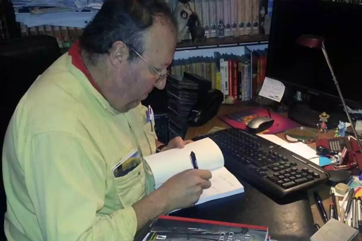 Foto de perfil de Miguel Aracil sentado en su escritorio firmando uno de sus libros