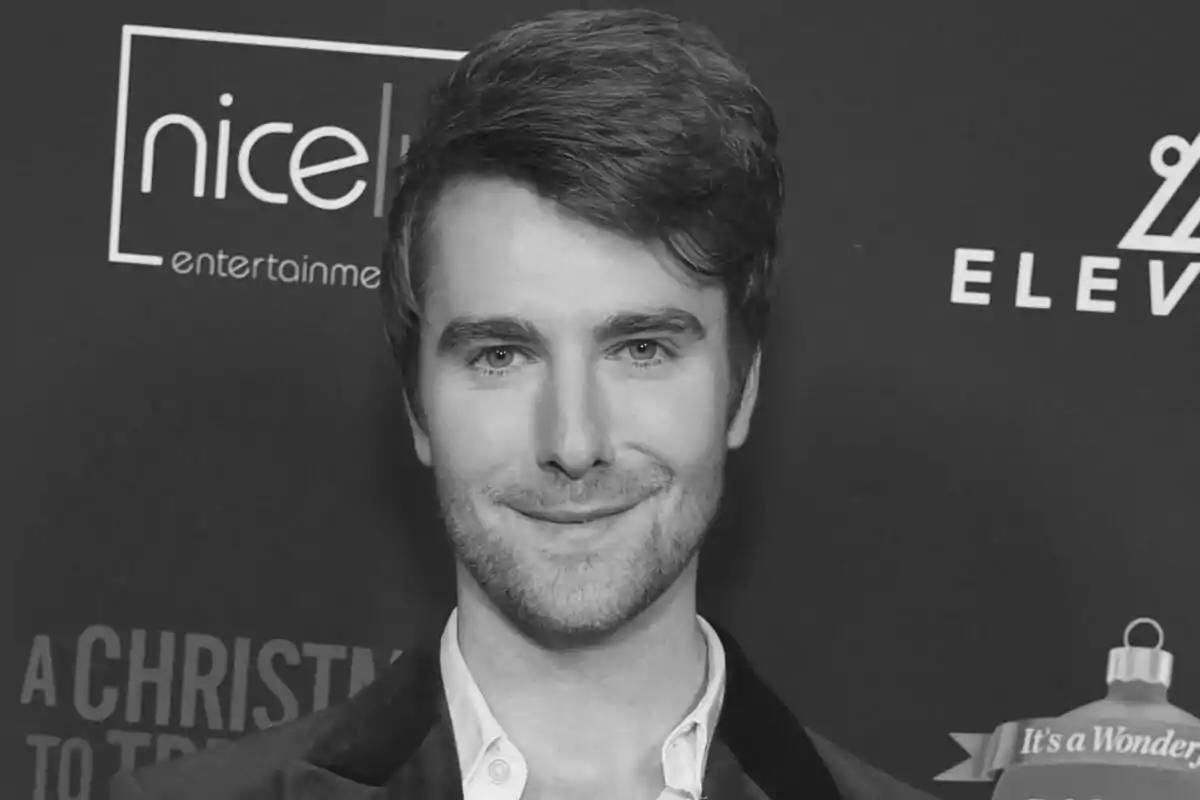 Fotografía en blanco y negro de Mike Heslin sonriente con barba ligera y cabello peinado hacia un lado, posando en un photocall.