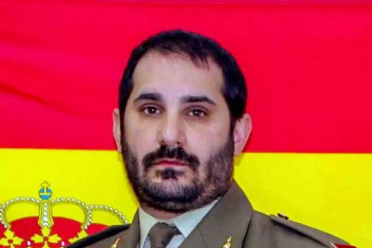 Primer plano del militar Iván Mejuto Rodríguez con rostro muy serio y la bandera de España de fondo