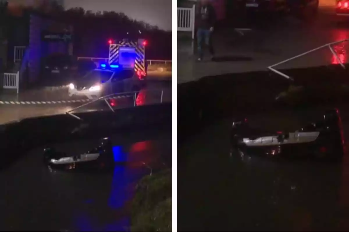 Un coche volcado en un cuerpo de agua mientras un vehículo de emergencia con luces encendidas está cerca en una carretera mojada.