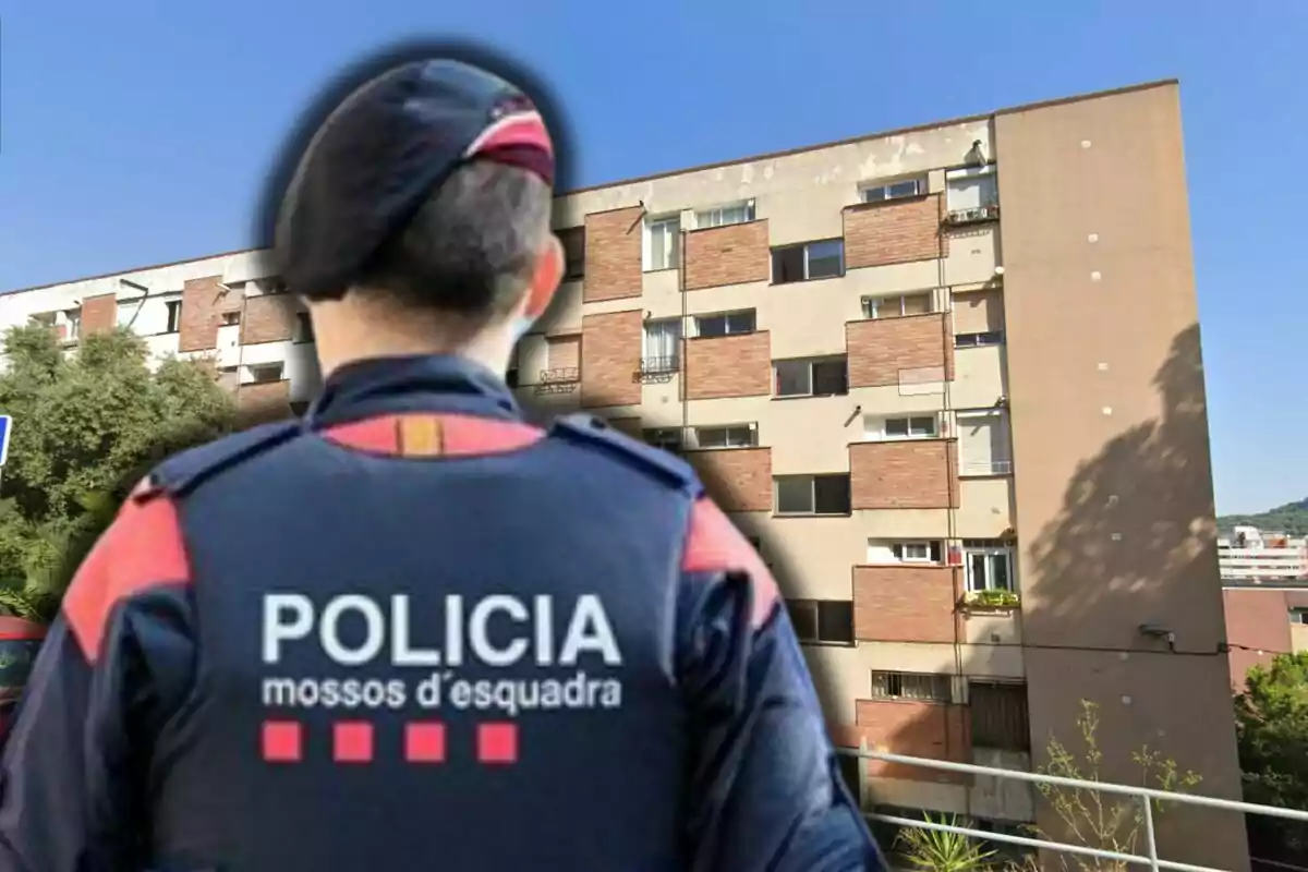 Agente de los Mossos d'Esquadra de espaldas frente a un edificio de apartamentos en un día soleado
