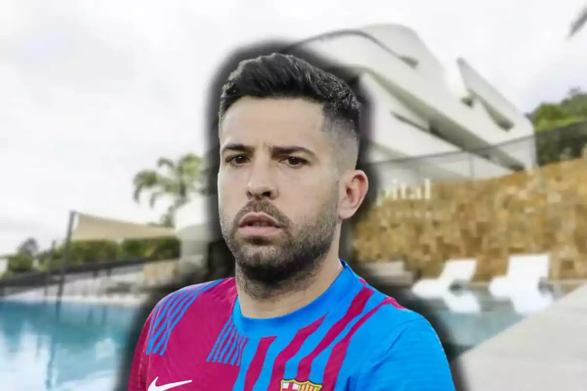 Jordi Alba con camiseta de fútbol azul y roja frente a una piscina y un edificio moderno.