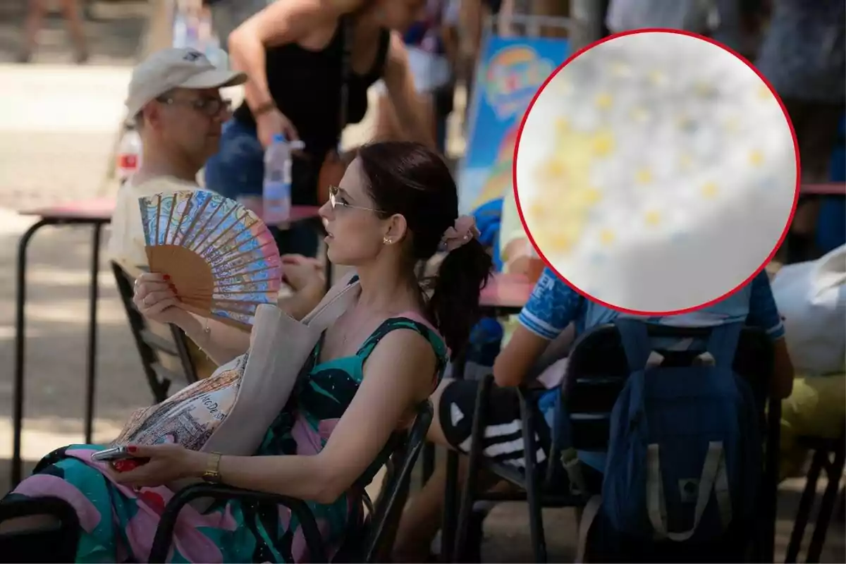 Una mujer sentada en una silla se abanica mientras sostiene un teléfono móvil, con varias personas sentadas alrededor en un entorno al aire libre.