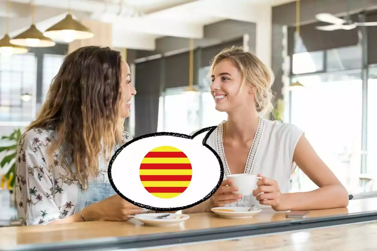 Dos mujeres sentadas en una cafetería conversando y sonriendo, con una burbuja de diálogo que contiene una bandera con rayas rojas y amarillas.