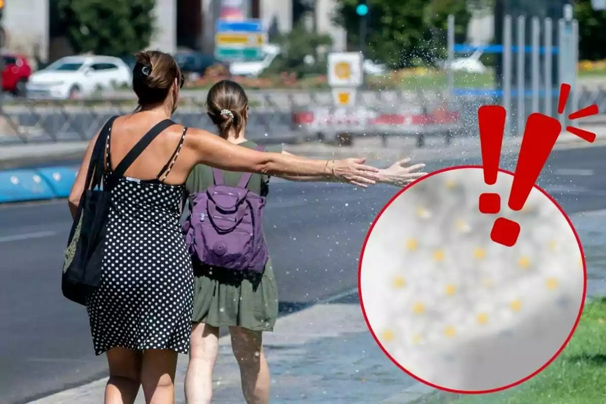 Dos personas caminando por la calle mientras una de ellas extiende el brazo para protegerse de una salpicadura de agua.