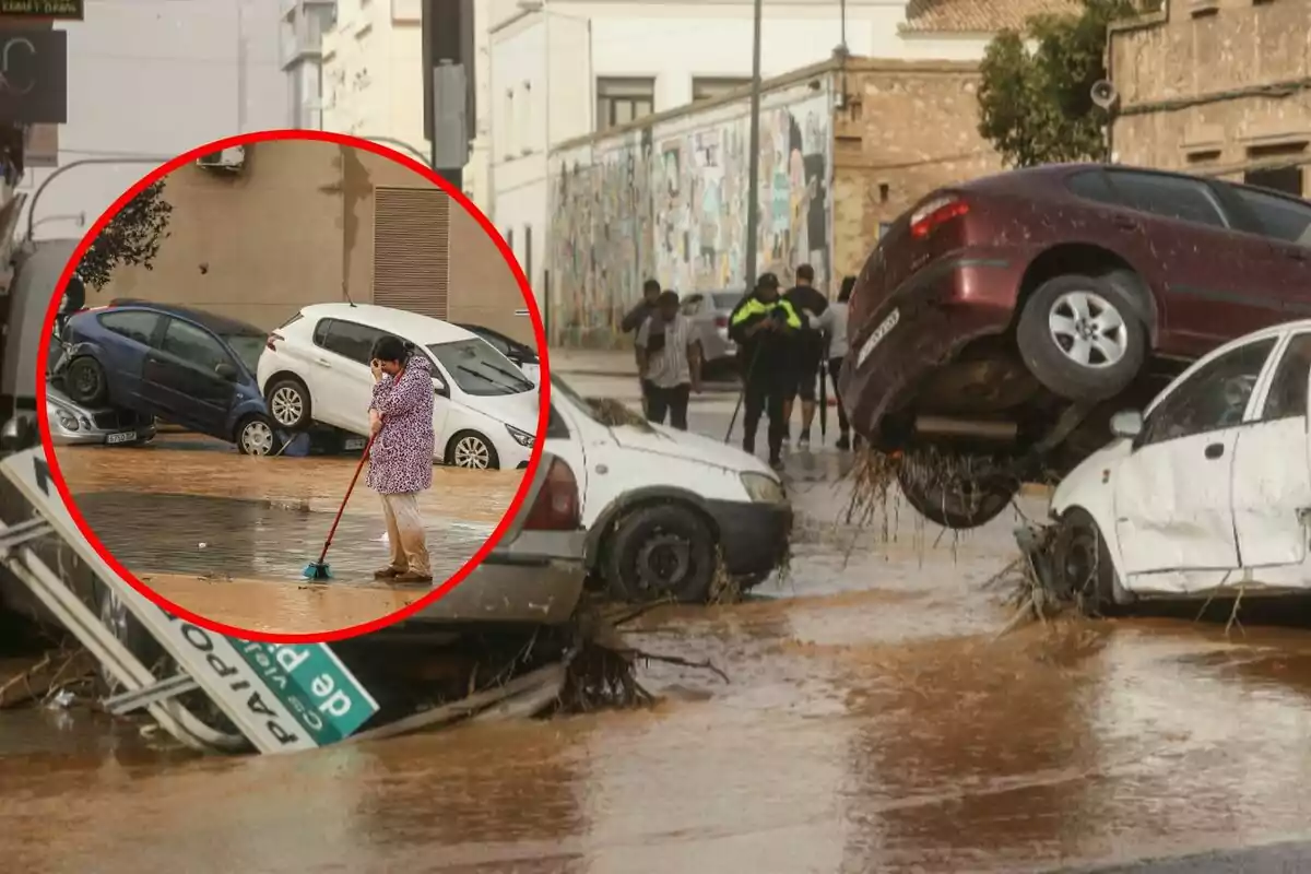 Una persona barre el agua en una calle inundada mientras varios coches están apilados debido a la fuerza del agua.