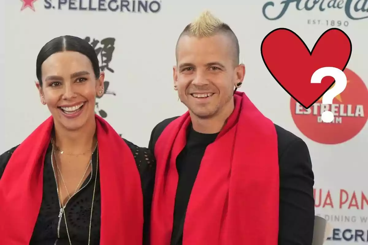 Cristina Pedroche y Dabiz Muñoz sonriente con bufandas rojas posando frente a un fondo con logotipos y un corazón con signo de interrogación.