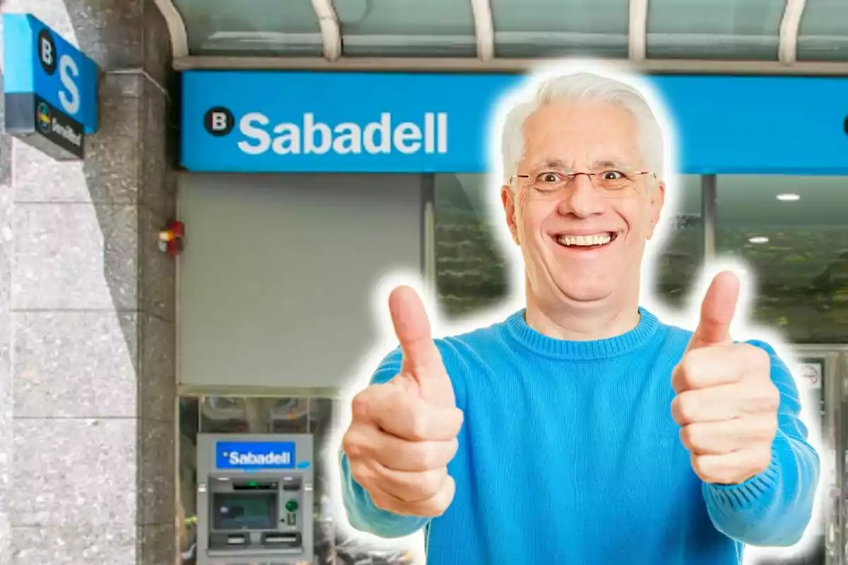 Un hombre mayor sonriente con pulgares arriba frente a un cajero automático del banco Sabadell.