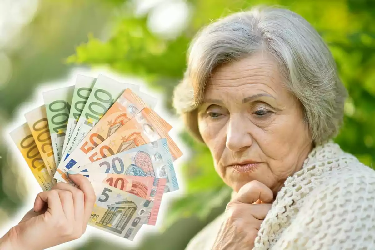 Una mujer mayor con expresión pensativa y preocupada, con una mano sosteniendo varios billetes de euro en primer plano.