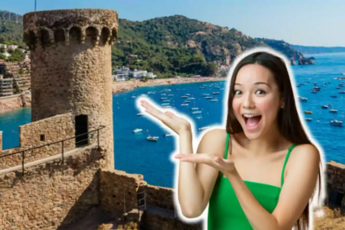 Una mujer sonriente con un vestido verde señala hacia una torre de piedra junto a un mar lleno de barcos y un paisaje montañoso al fondo.