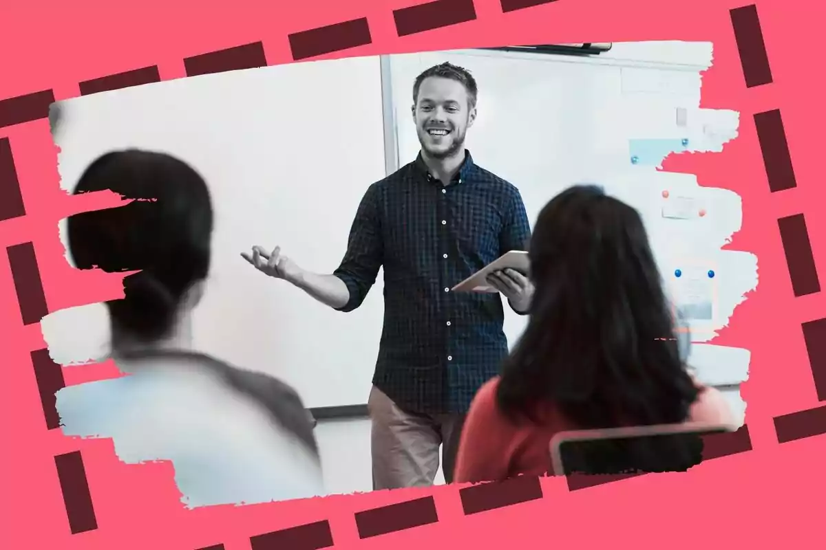Un hombre sonriente con una camisa a cuadros sostiene una tableta mientras habla frente a dos personas en un aula con un fondo decorativo en tonos rosados.