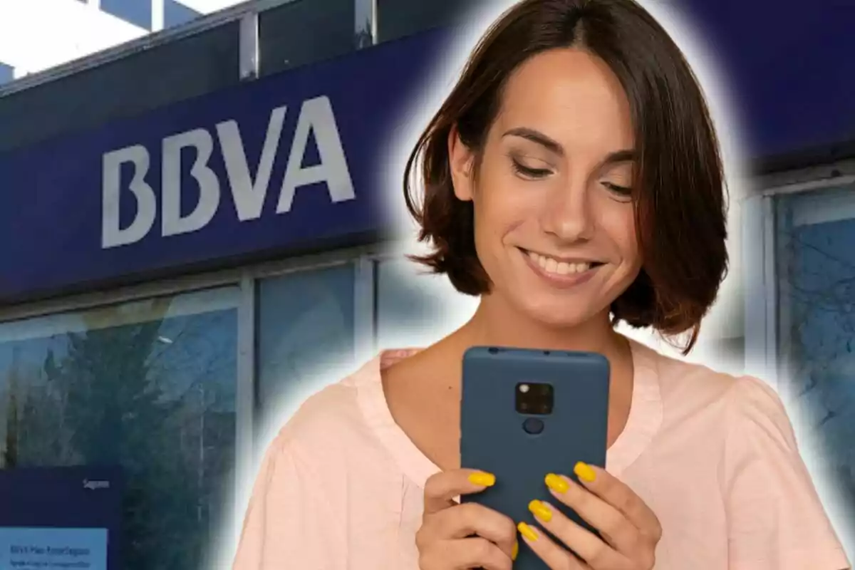 Una mujer sonriente con un teléfono móvil frente a un edificio del BBVA.