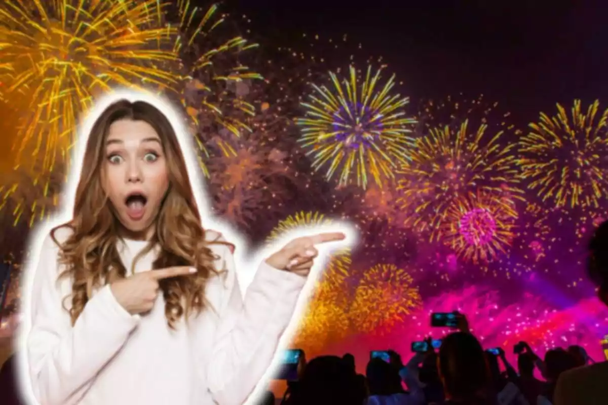 Una mujer con expresión de sorpresa y señalando hacia la derecha, con un fondo de fuegos artificiales coloridos en el cielo nocturno y una multitud de personas tomando fotos con sus teléfonos móviles.