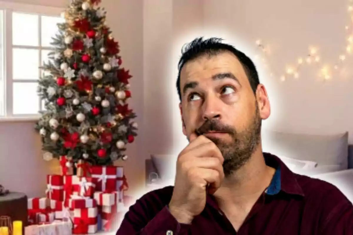 Hombre pensativo frente a un árbol de Navidad decorado con regalos al pie.