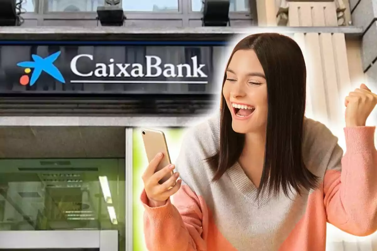 Una mujer sonriente sostiene un teléfono móvil frente a una sucursal de CaixaBank.