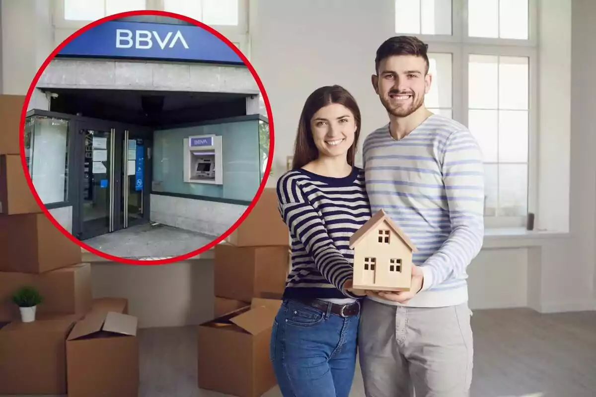 Una pareja sonriente sostiene una casa en miniatura en una habitación con cajas de mudanza, con una imagen insertada de una sucursal del banco BBVA.