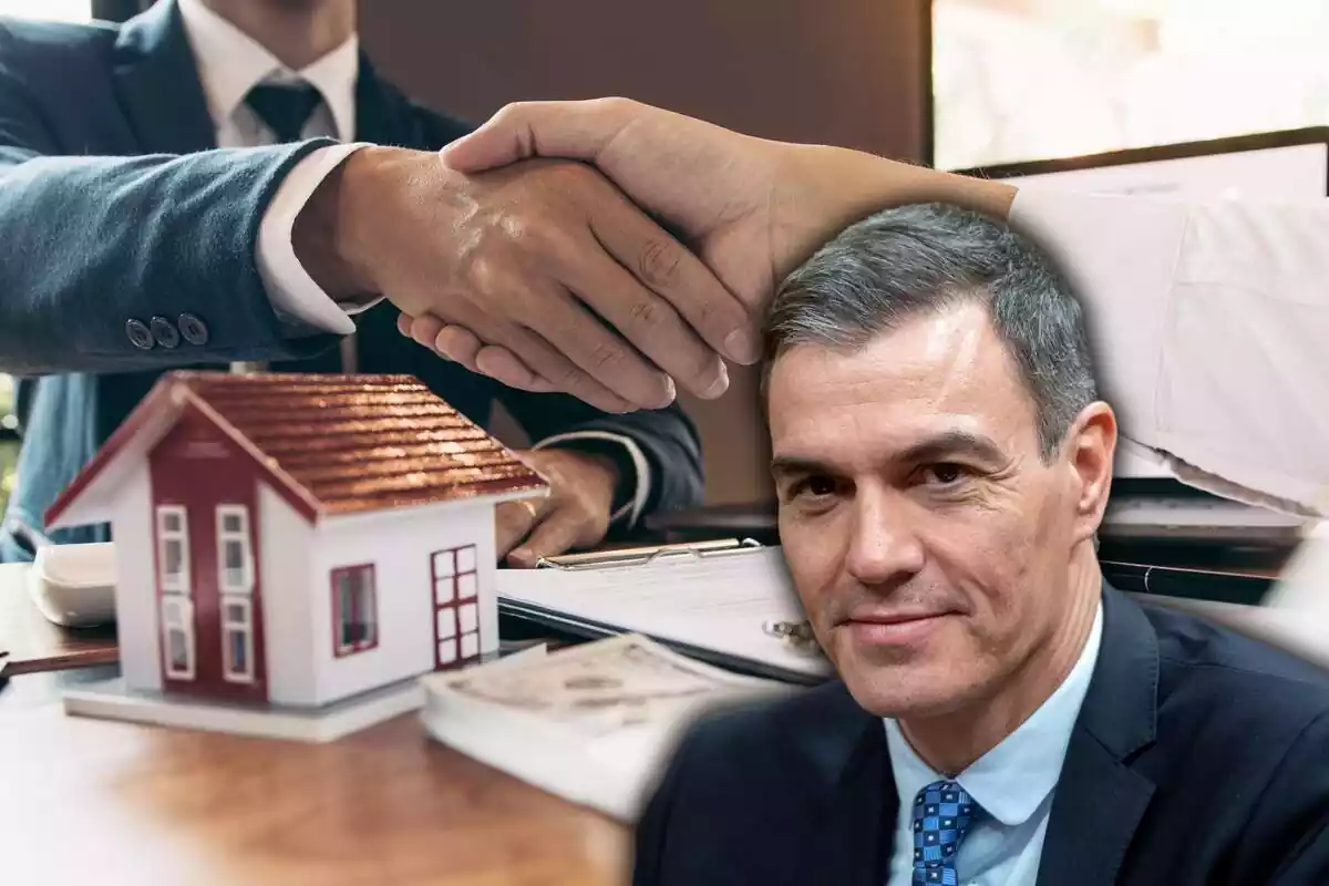 Dos personas se dan la mano, en una mesa con papeles y una casa en miniatura, con una imagen de Pedro Sánchez en el lateral derecho
