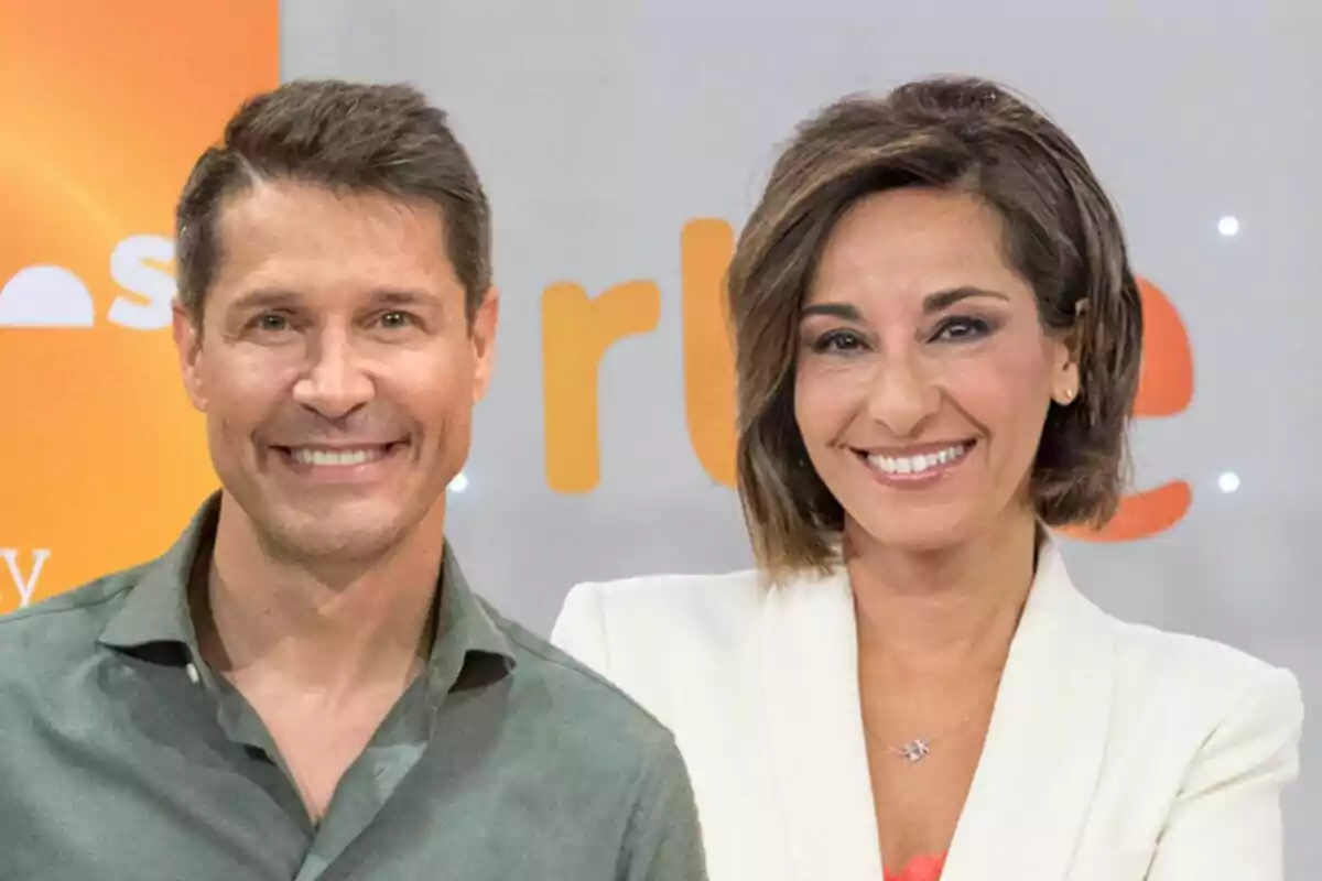 Jaime Cantizano y Adela González sonrientes posando frente a un fondo con letras naranjas.