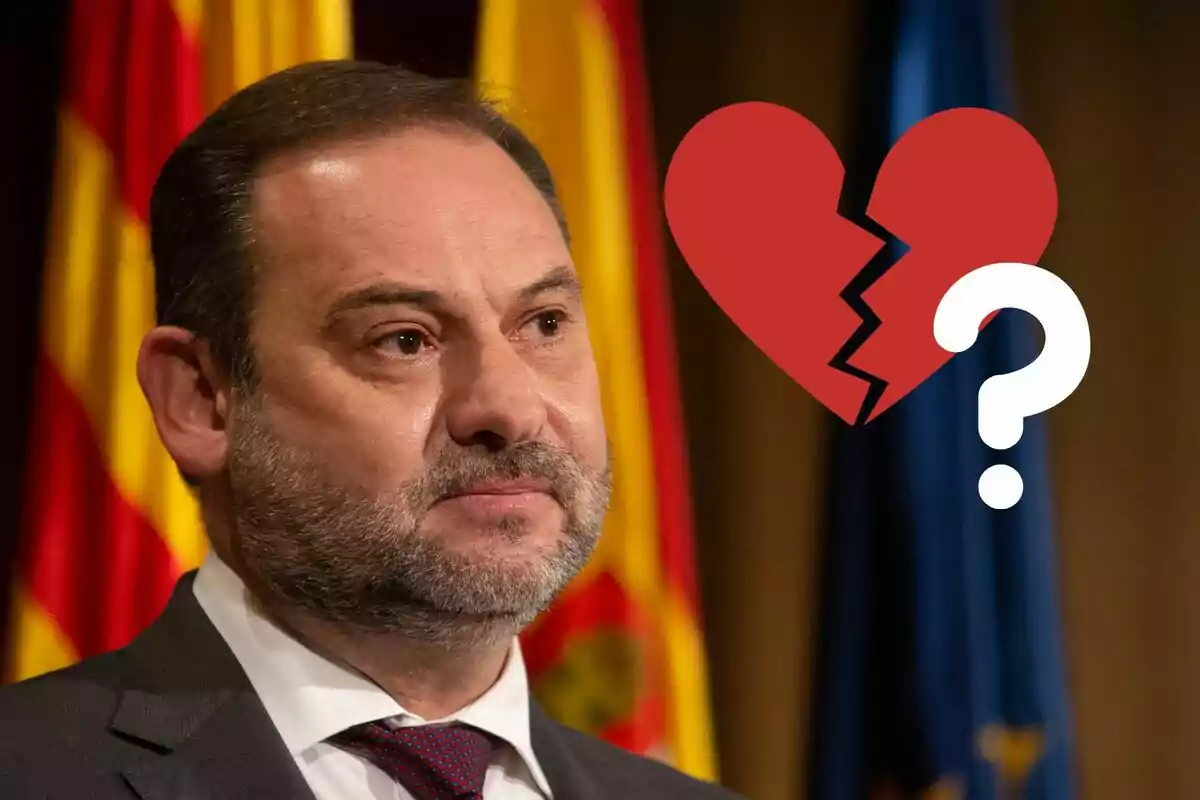 José Luis Ábalos con expresión seria frente a banderas con un corazón roto y un signo de interrogación superpuestos.