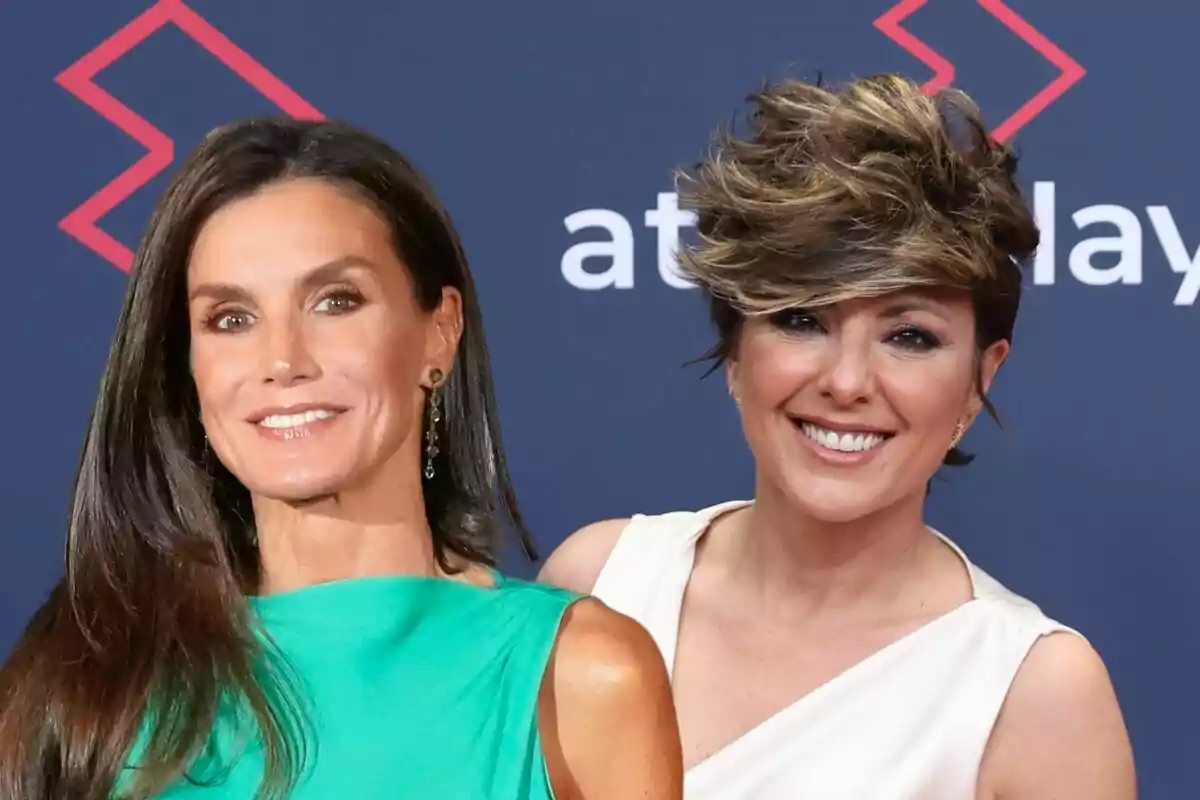 Letizia y Sonsoles Ónega sonrientes posan juntas en un evento con fondo azul y detalles geométricos rojos.