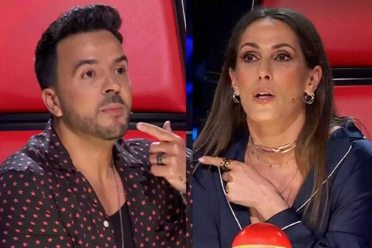 Dos personas sentadas en sillas rojas de La Voz, Luis Fonsi con una camisa negra con estrellas rojas y Malú con una blusa azul, ambas señalando con el dedo índice.