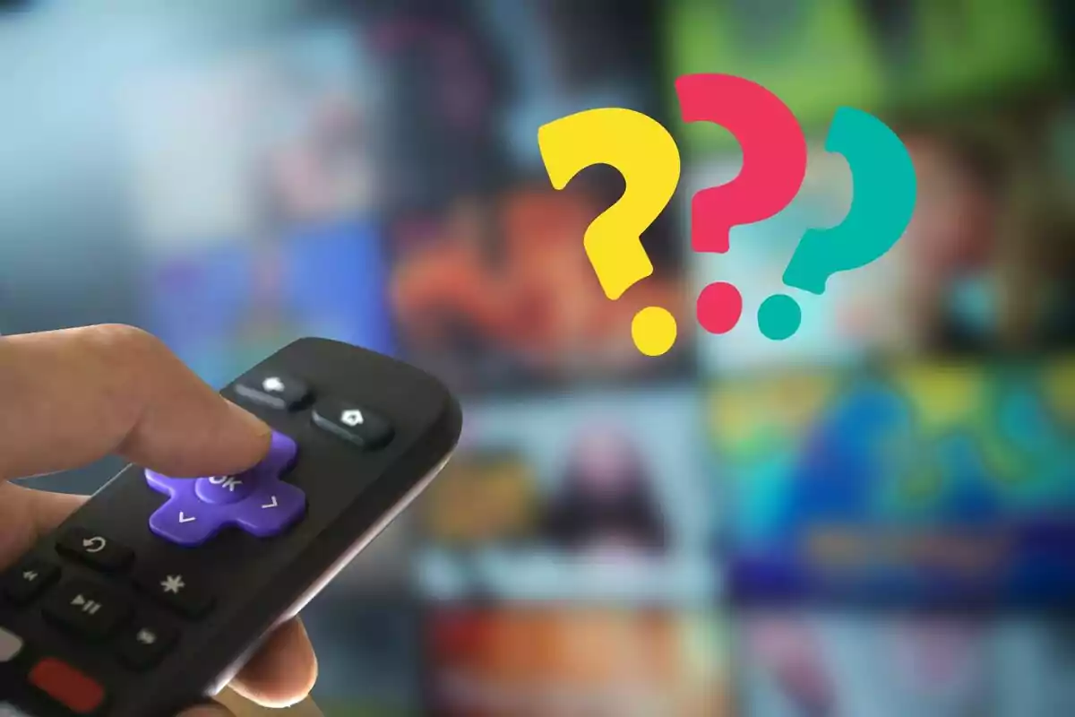 Una mano sosteniendo un control remoto frente a una pantalla borrosa con signos de interrogación de colores flotando. Una mano sosteniendo un control remoto frente a una pantalla borrosa con signos de interrogación de colores flotando.
