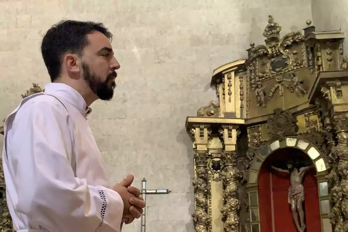Un hombre con vestimenta religiosa blanca está de perfil en una iglesia con un altar ornamentado al fondo. Un hombre con vestimenta religiosa blanca está de perfil en una iglesia con un altar ornamentado al fondo.